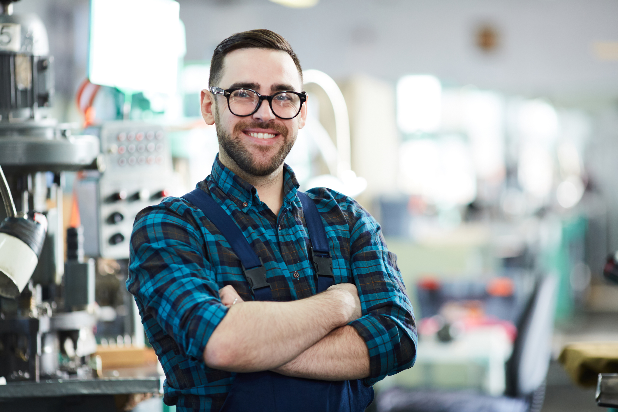 Waist up portrait of cheerful factory worker looking at camera while posing in workshop standing with arms crossed